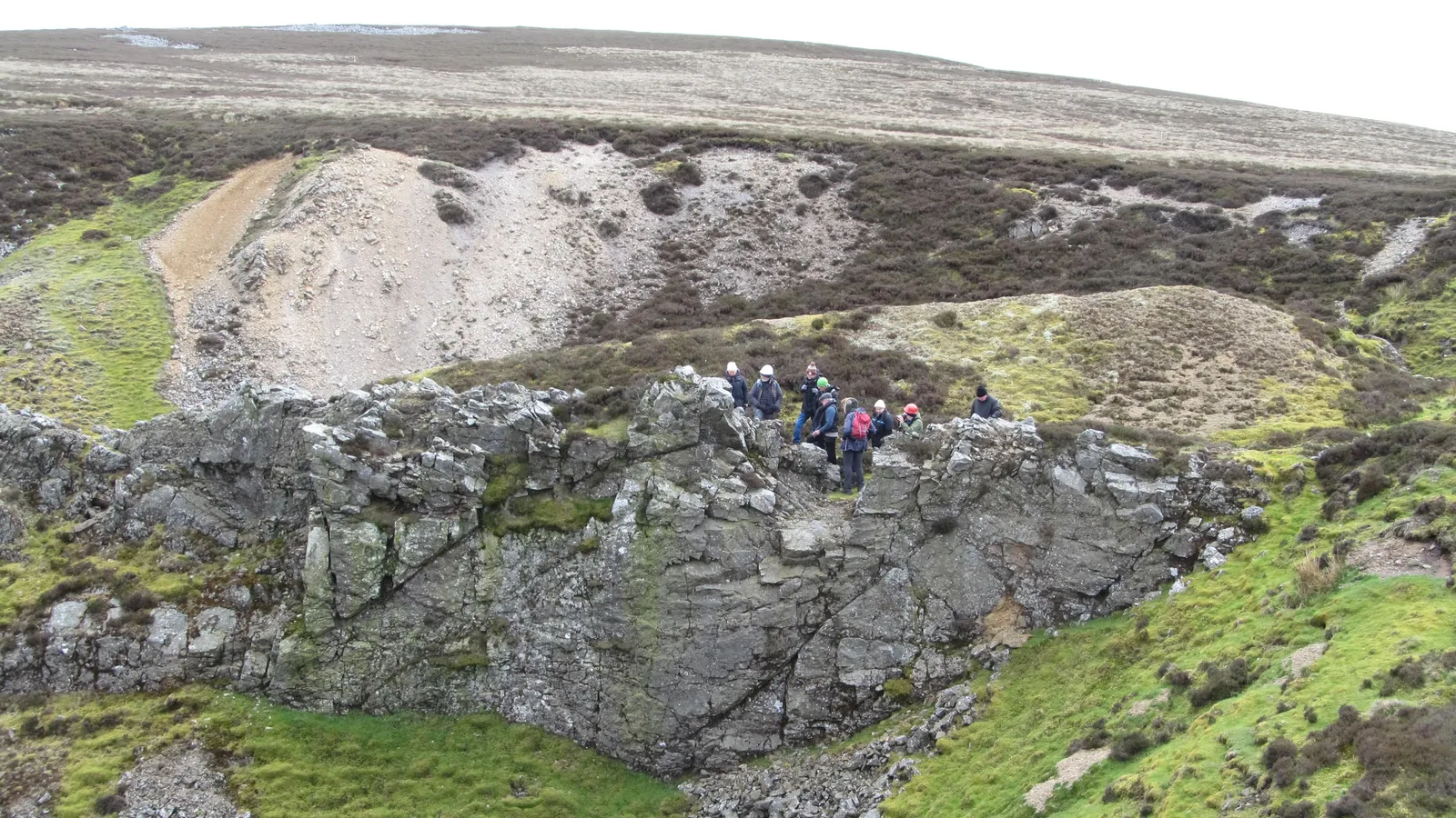 Group of geologists, some in hard hats, standing on a grey rock outcrop on moorland