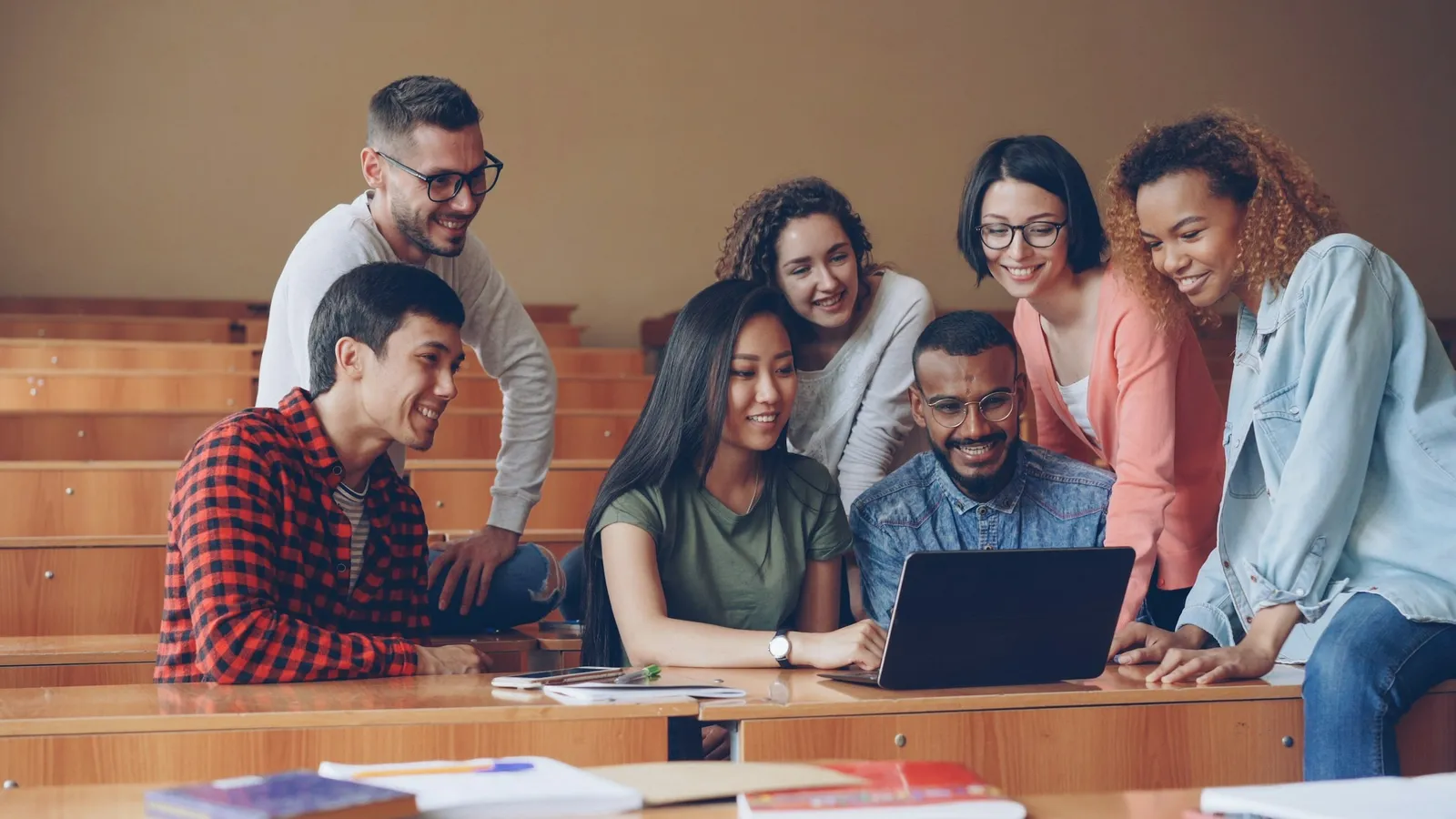 Group of students discussing a problem together around a laptop in a lecture hall