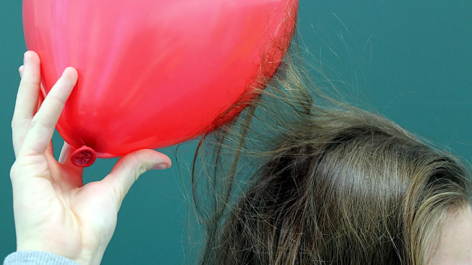 Hand holding a red balloon beside a head, strands of hair rising toward it