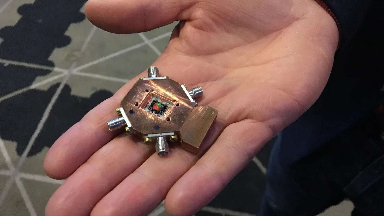 Hand holding a small superconducting quantum processor in a copper mount with connectors