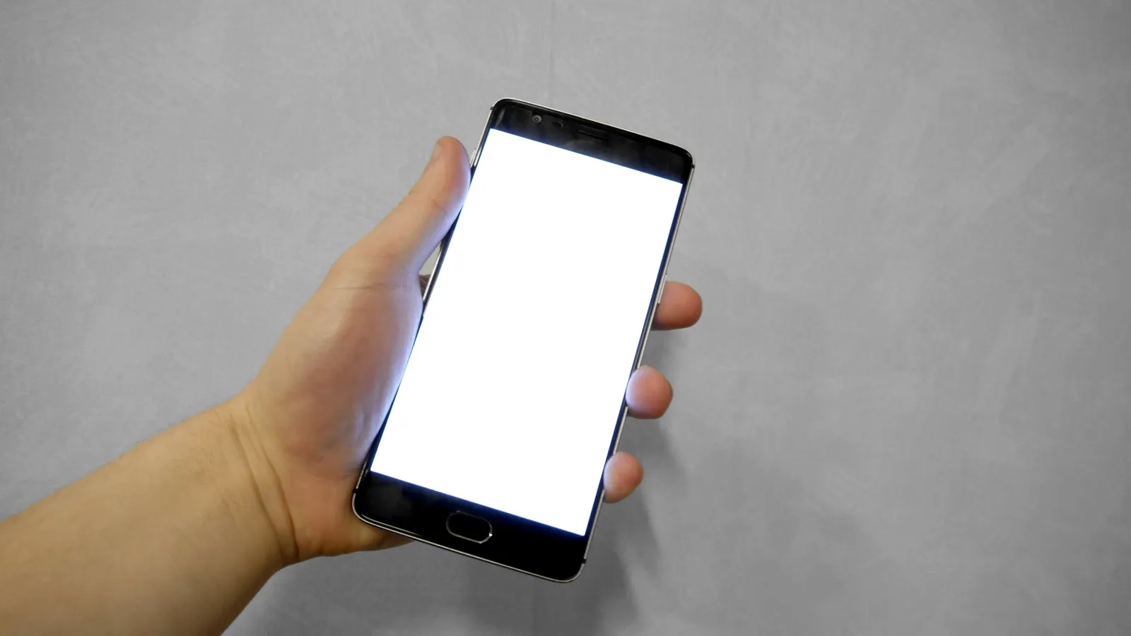 Hand holding a smartphone with a blank white screen against a grey wall