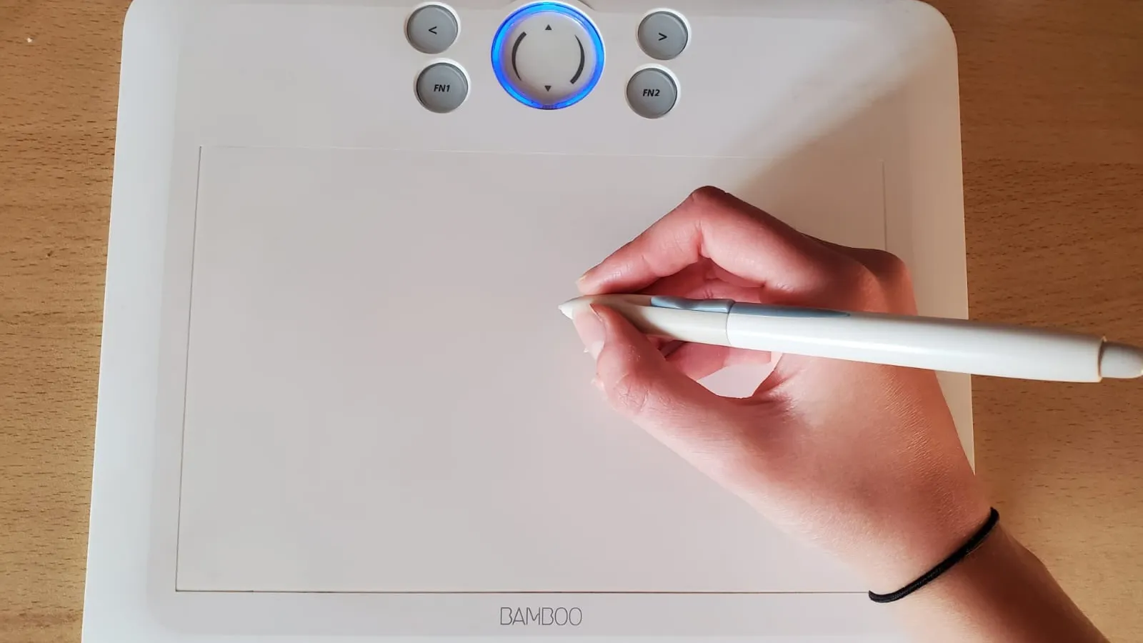 Hand holding a stylus and drawing on a white graphic tablet