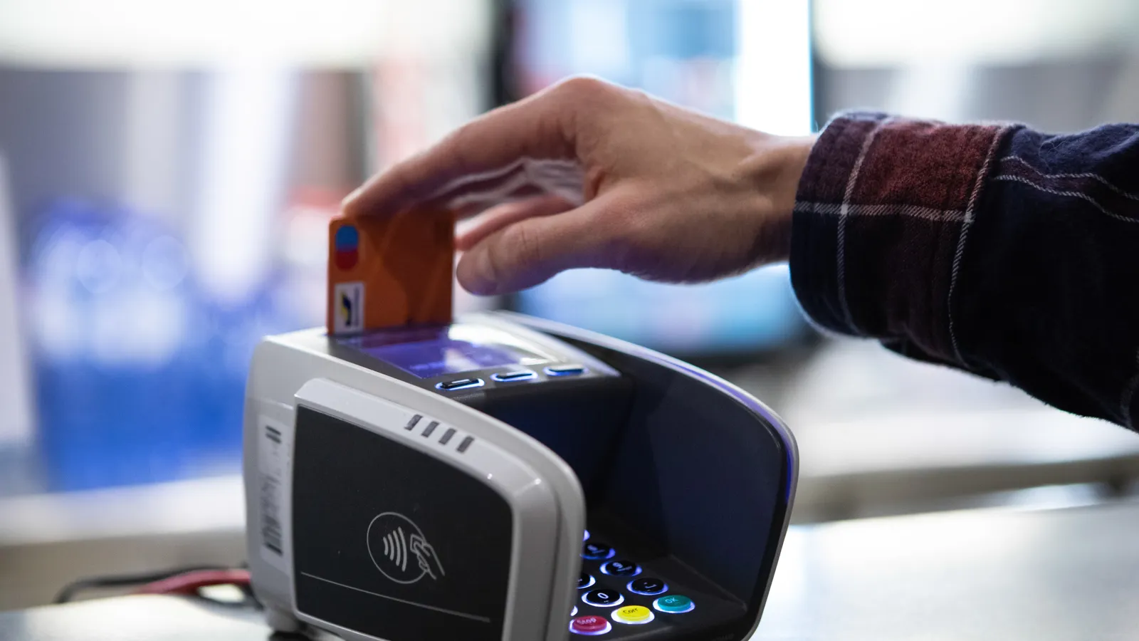 Hand inserting an orange card into a countertop card payment terminal