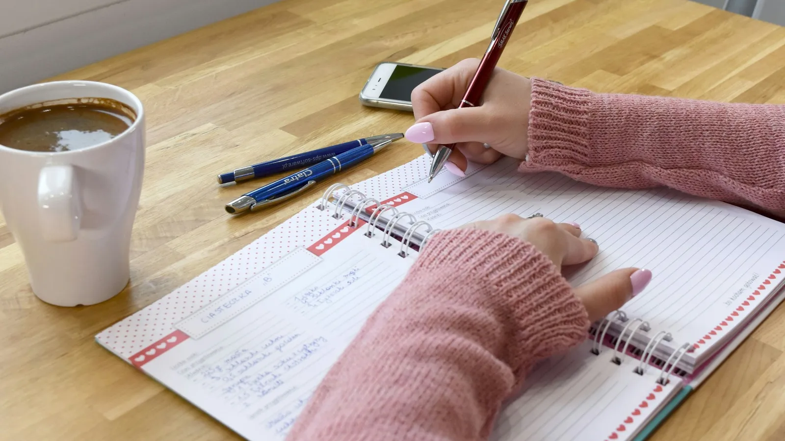 Hand writing in a notebook beside a cup of coffee