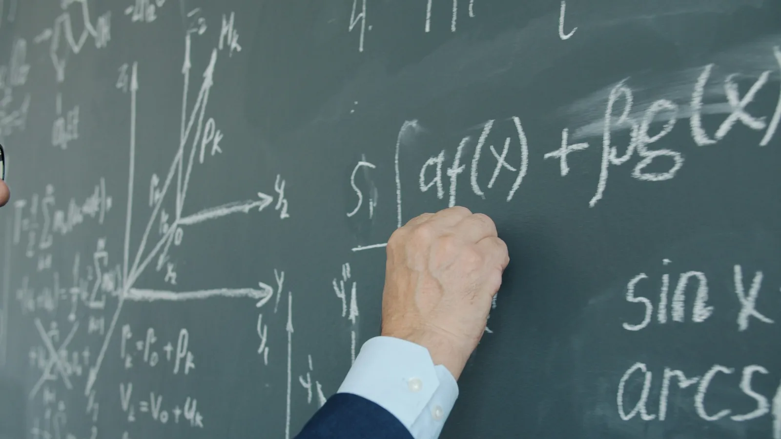 Hand writing integrals on a green chalkboard