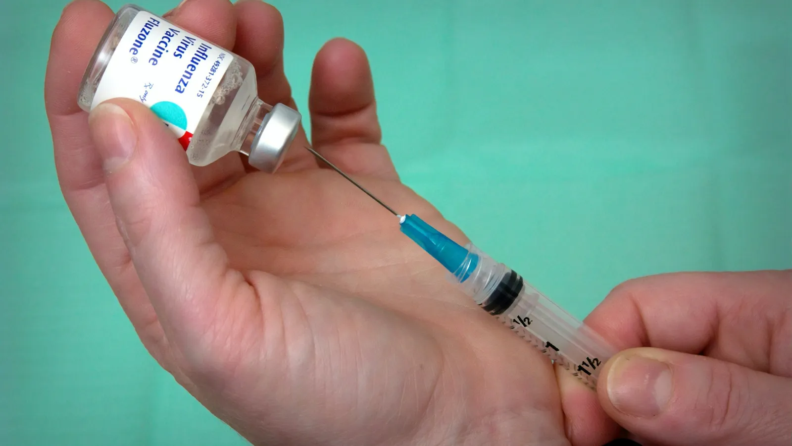 Hands drawing a dose from a small vial into a syringe