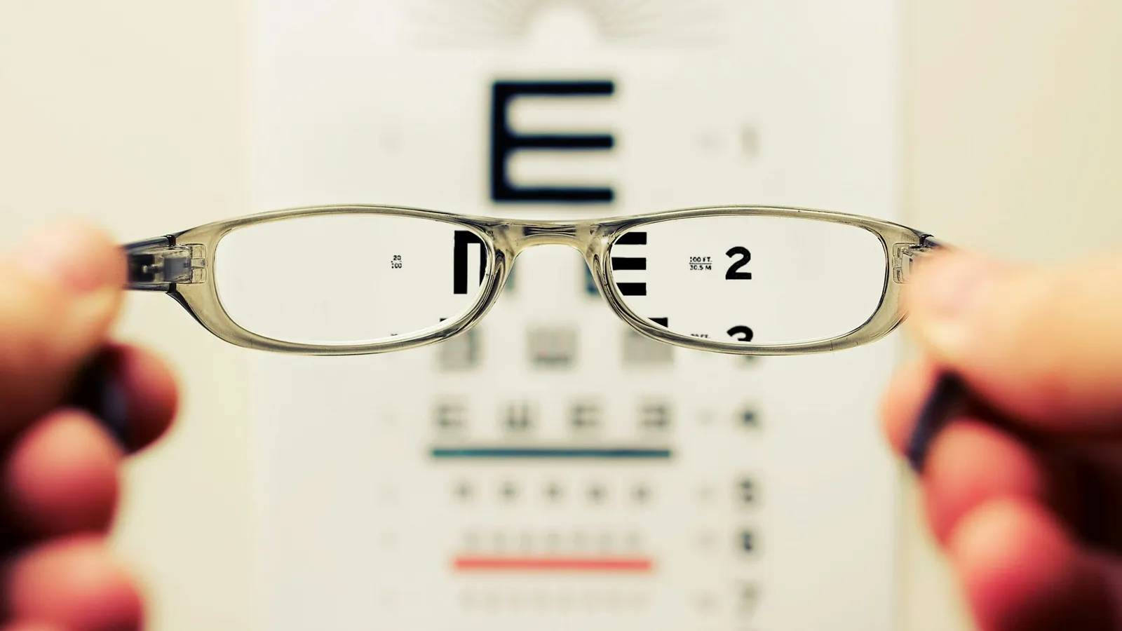 Hands holding glasses up in front of an eye chart