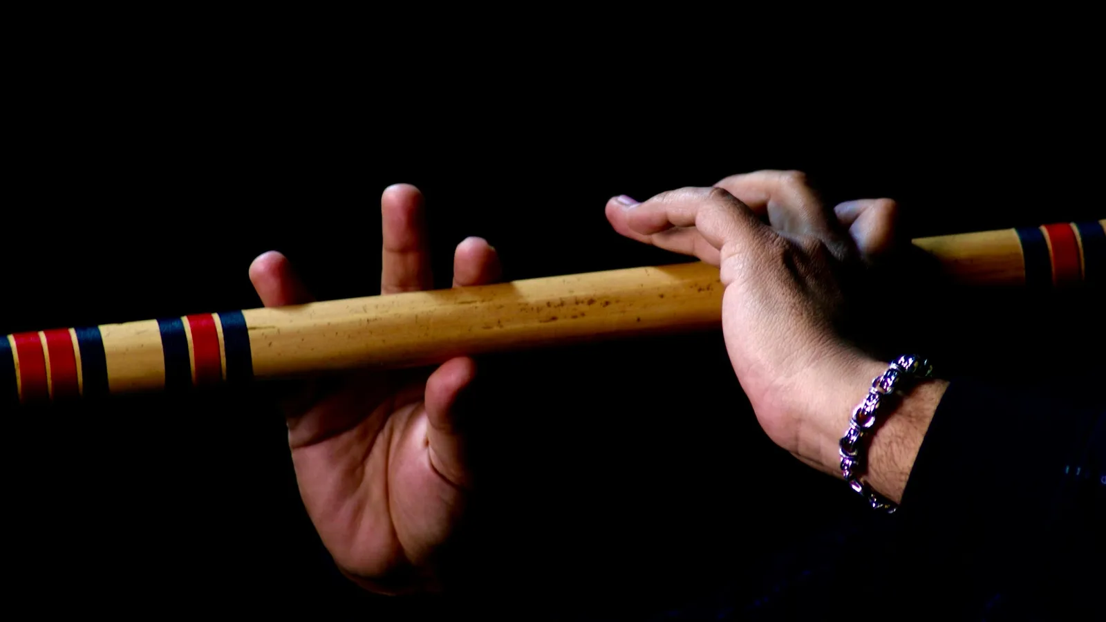 Hands playing a bamboo flute against a black background