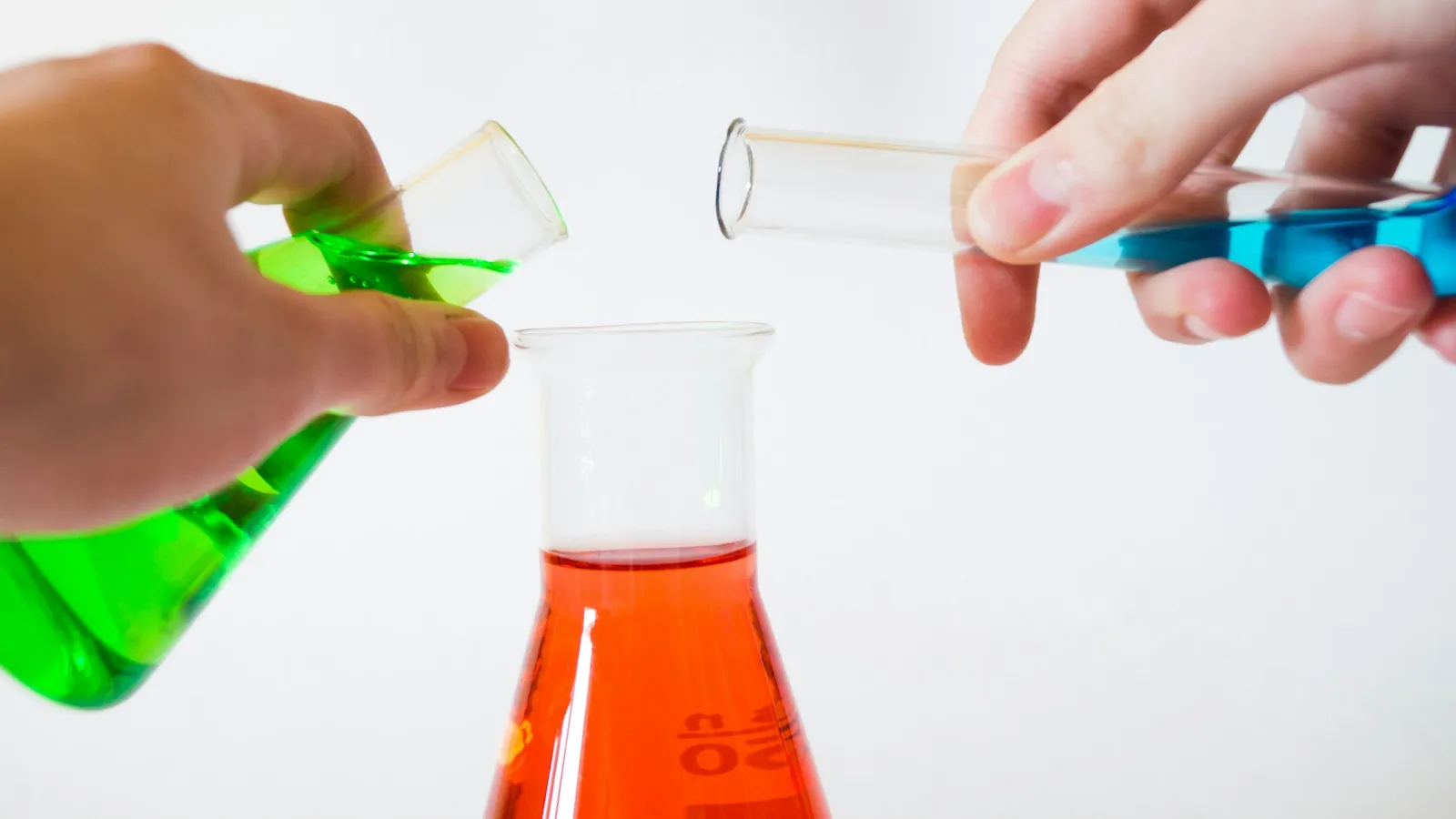 Hands pouring coloured liquids between laboratory flasks