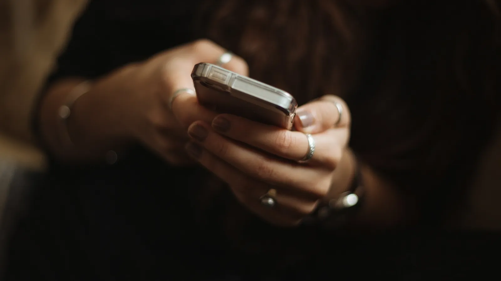Hands scrolling on a smartphone in dim light