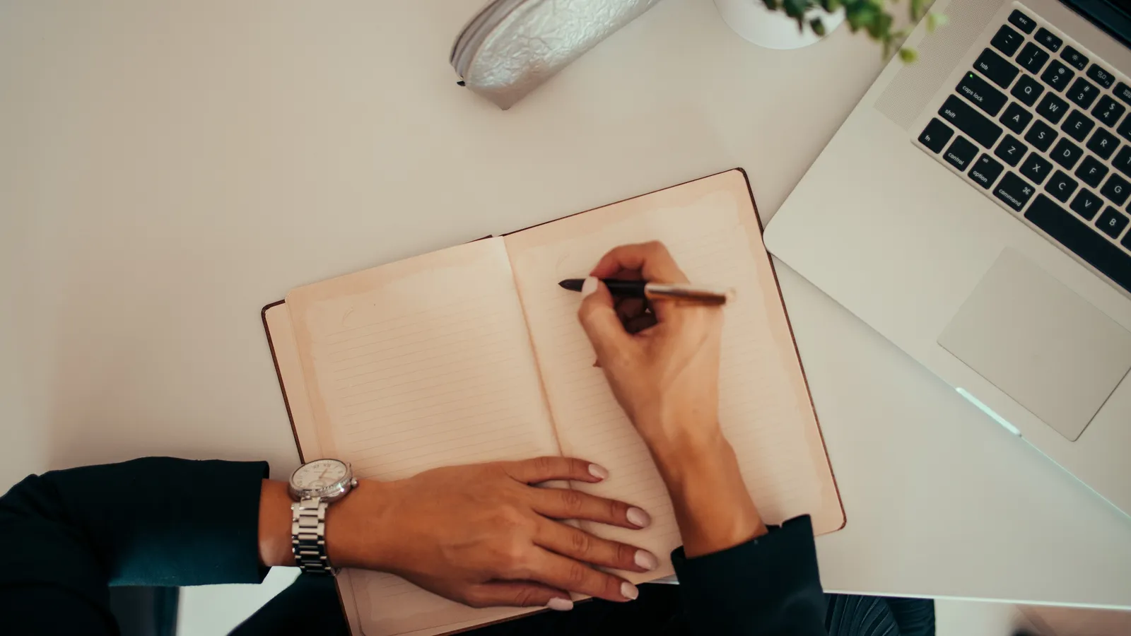 Hands starting to write on a blank notebook page beside a laptop