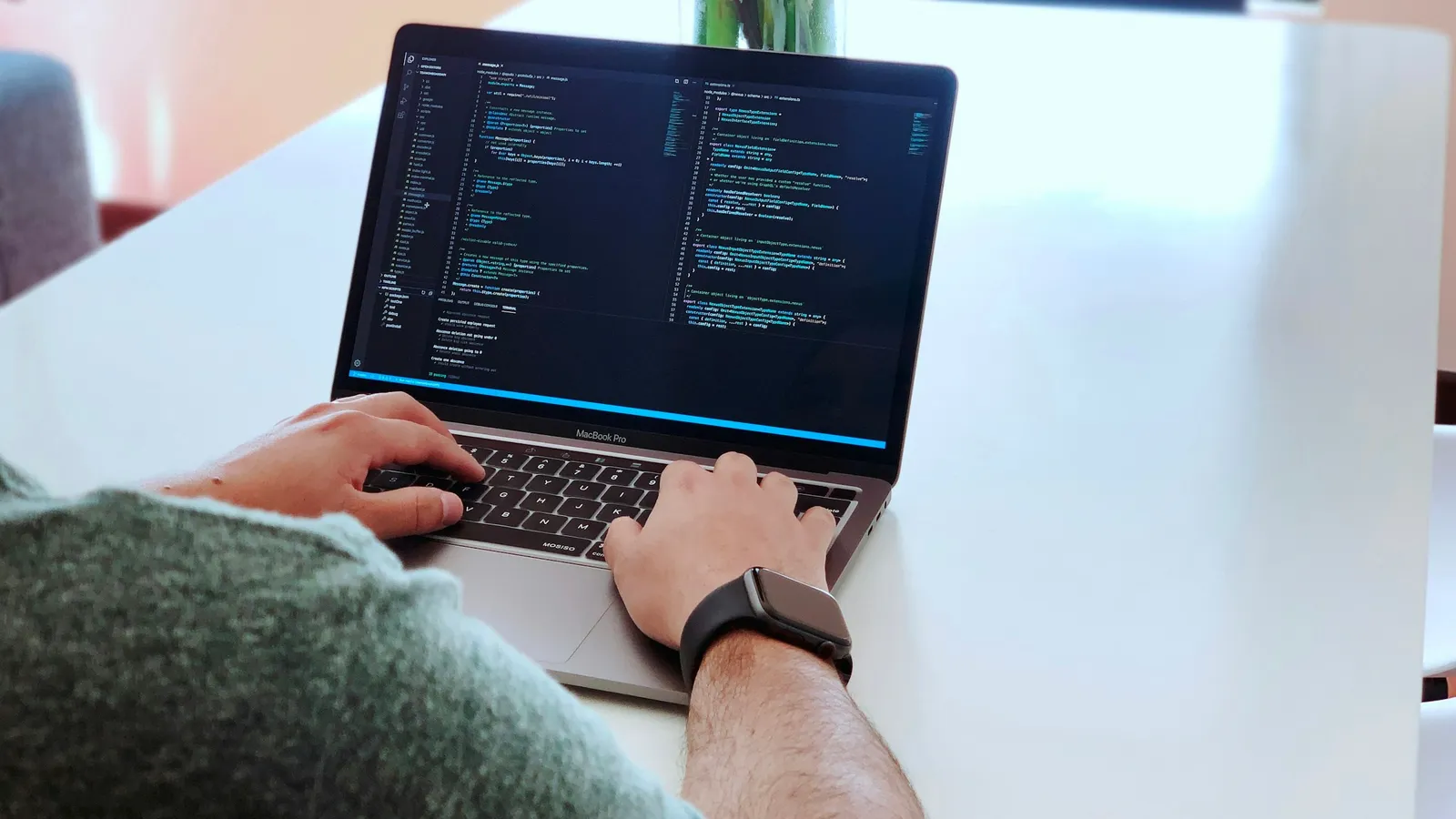 Hands typing code on a laptop at a white desk