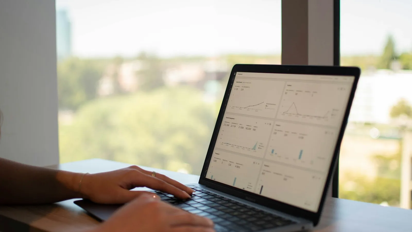 Hands typing on a laptop beside a window