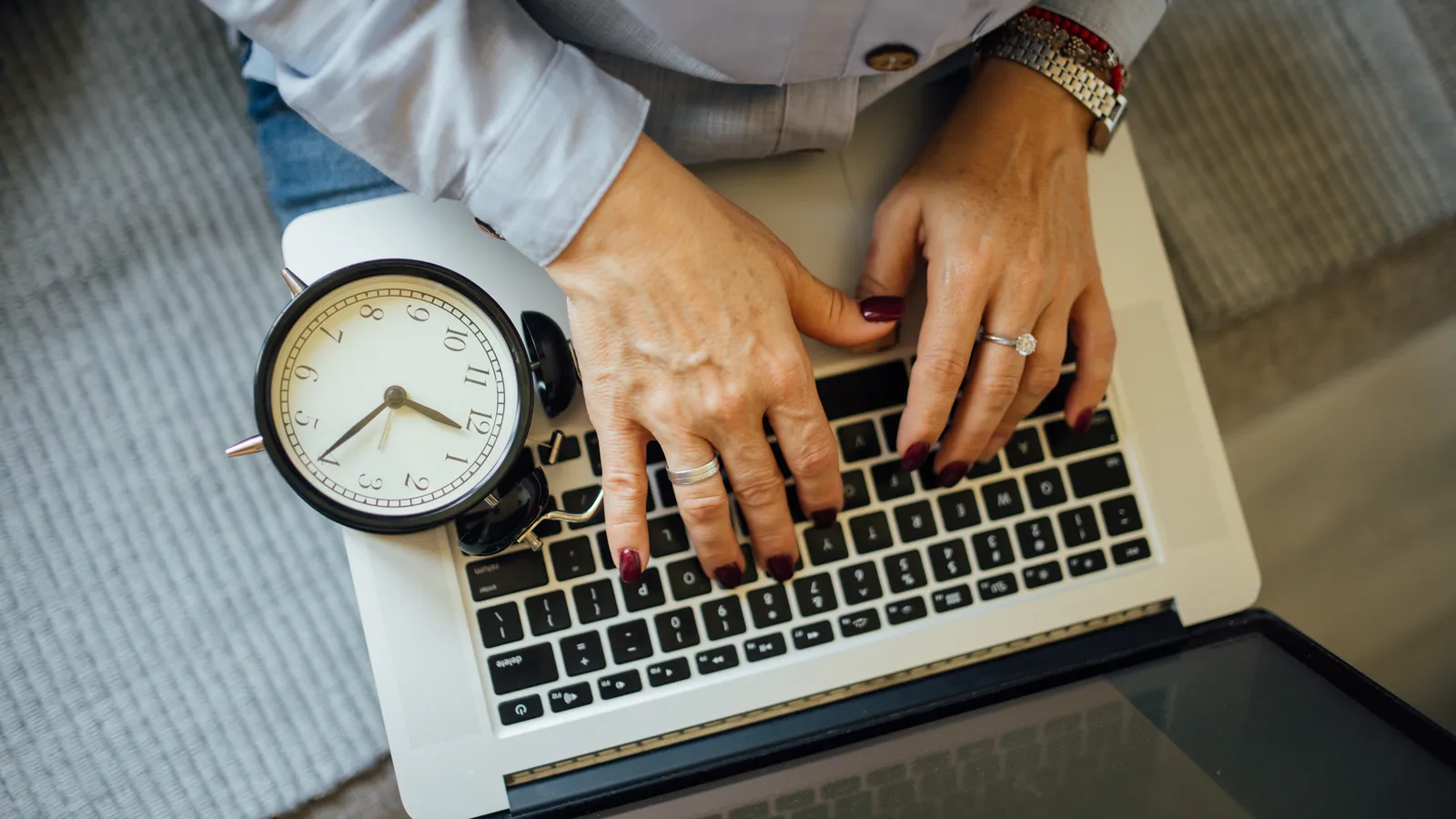Hands typing on a laptop keyboard beside a small analogue alarm clock