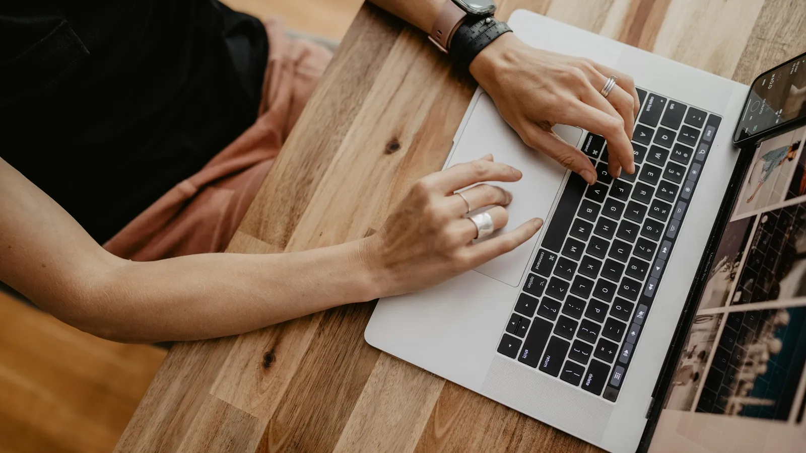 Hands typing on a laptop resting on a wooden table