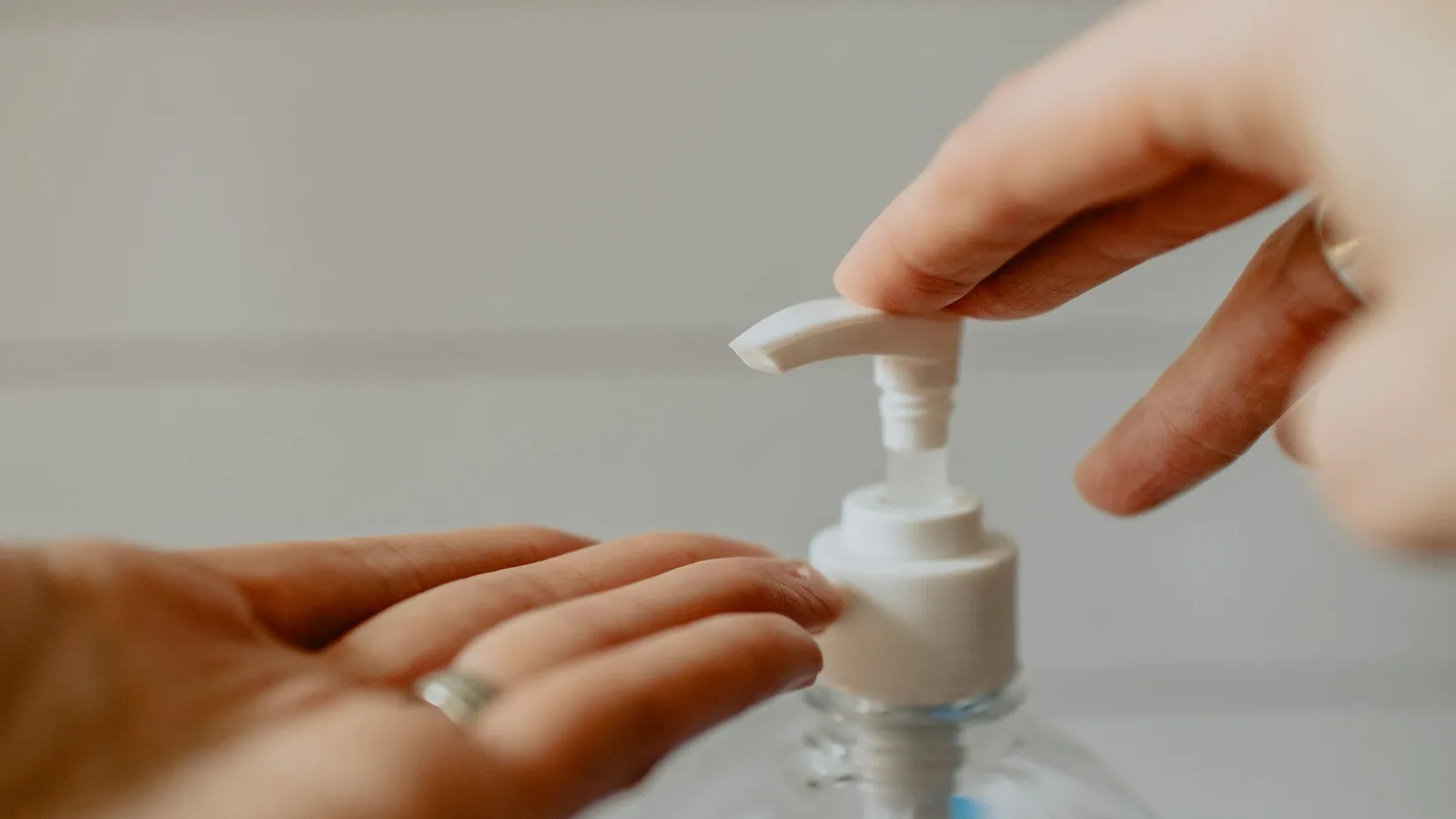 Hands using a pump bottle of hand sanitiser gel