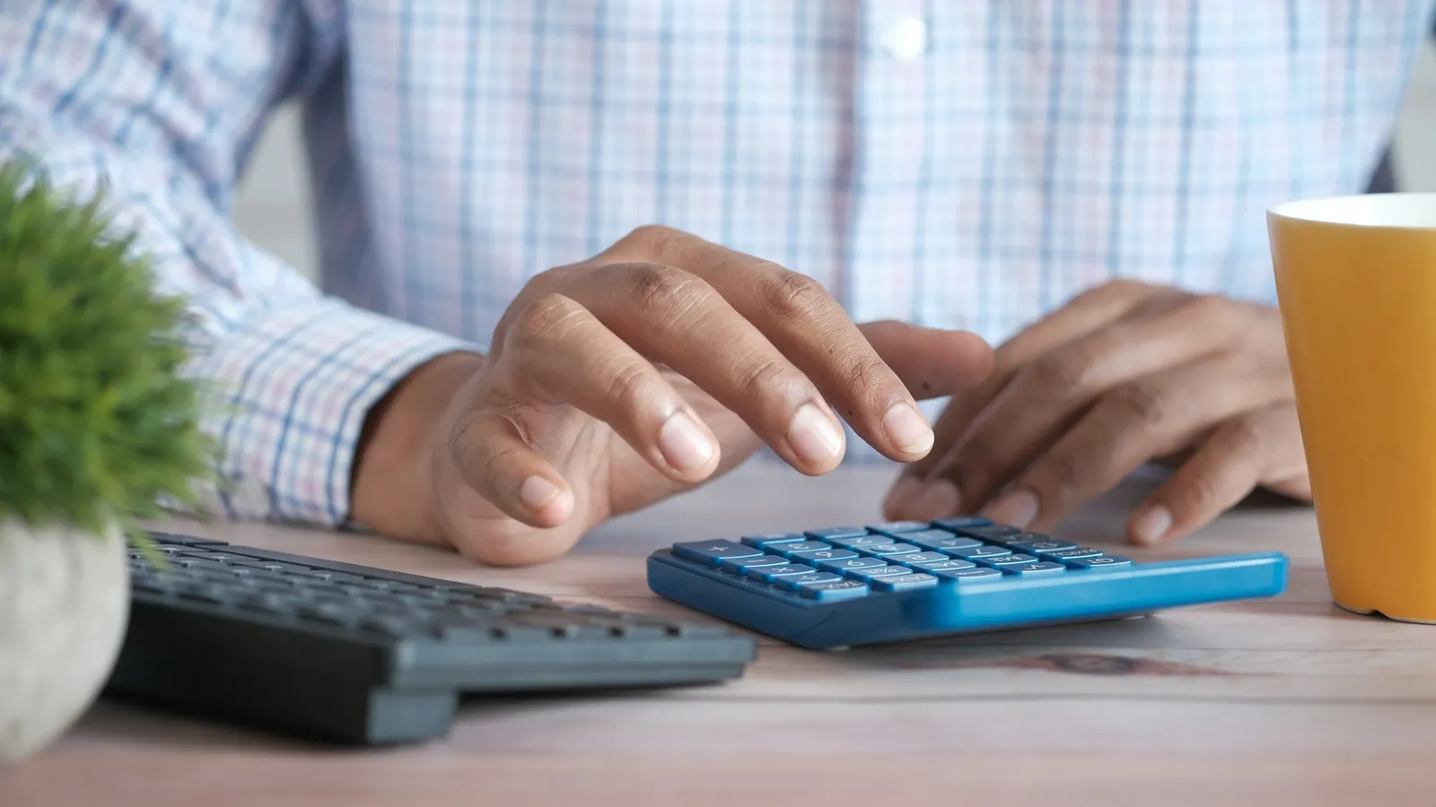 Hands working on a calculator at a desk beside a mug