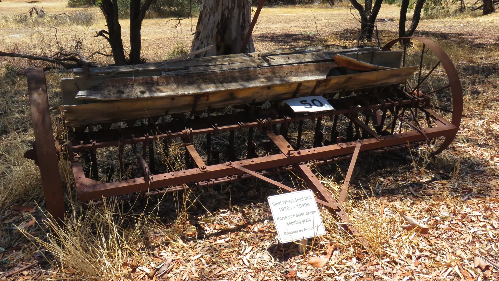 Historic steel-wheeled seed drill resting on dry grass