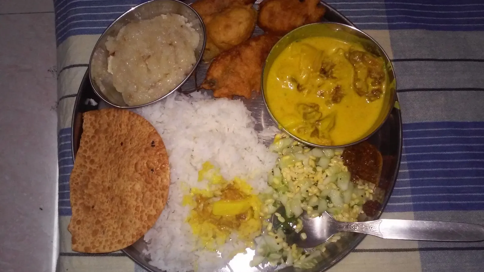 Home-cooked steel thali with rice, kadhi, pakodas, halwa, salad and papad