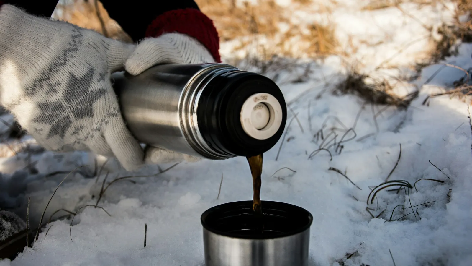 Hot drink being poured from a vacuum flask in the snow