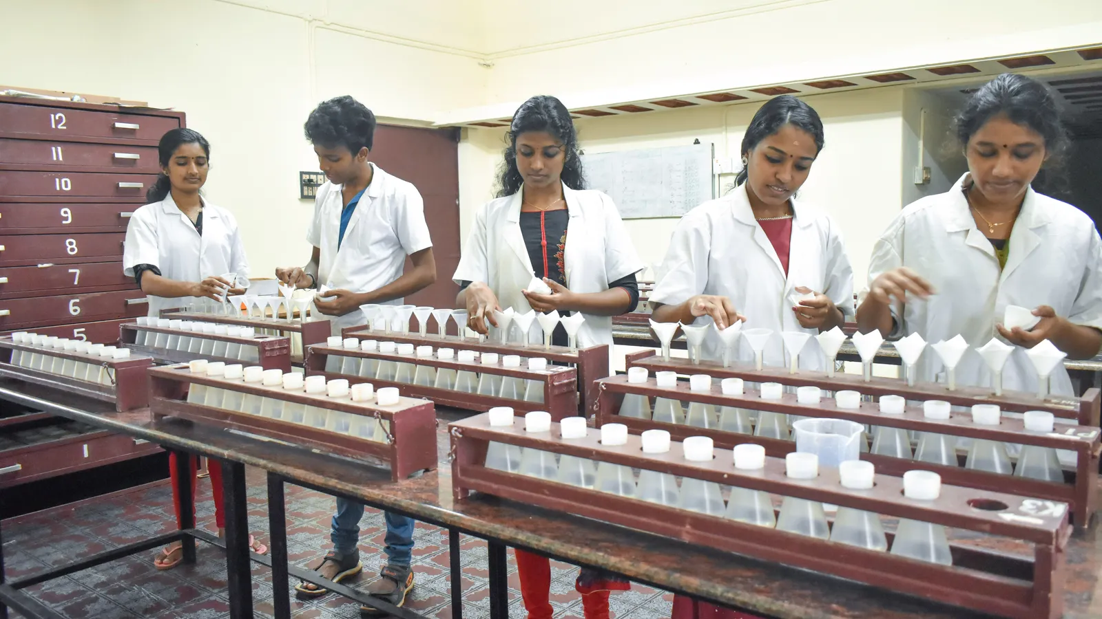 Lab workers in white coats setting filter papers into funnels in a soil testing laboratory