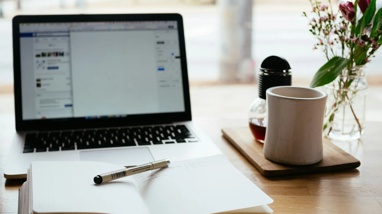 Laptop beside an open notebook and a pen on a wooden desk
