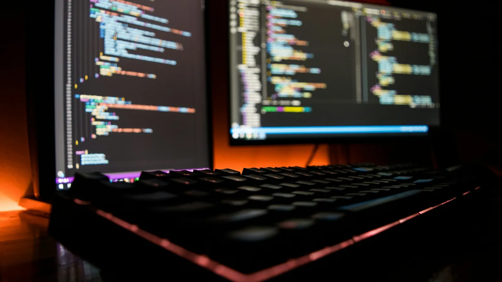 Lines of code on two screens above a lit keyboard