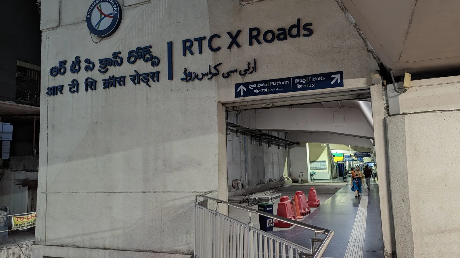 Lit entrance walkway of RTC X Roads metro station in Hyderabad at night, with a few people inside
