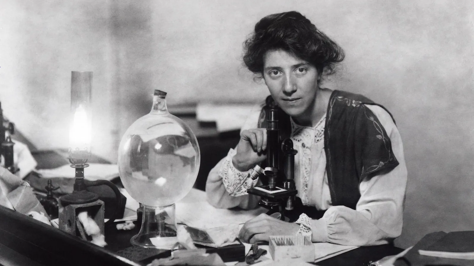 Marie Stopes at a microscope with slides, a lamp and a glass flask
