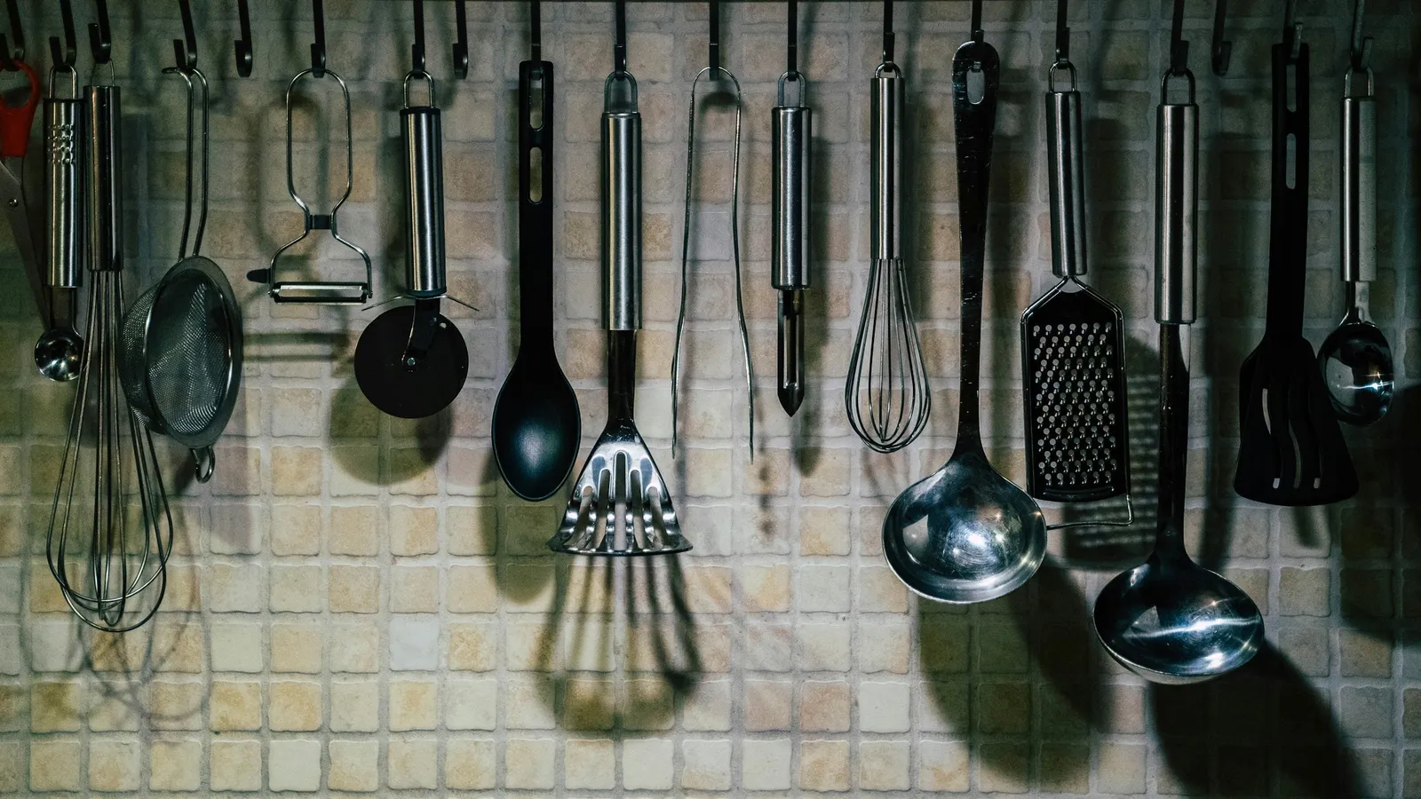 Metal kitchen utensils hanging against a tiled wall