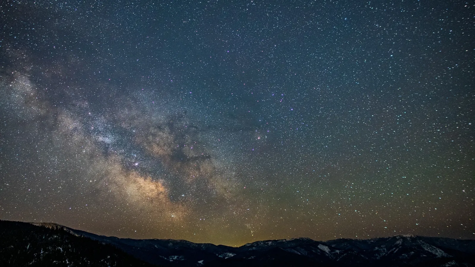 Milky Way and a faint meteor streak above dark, snow-dusted mountains