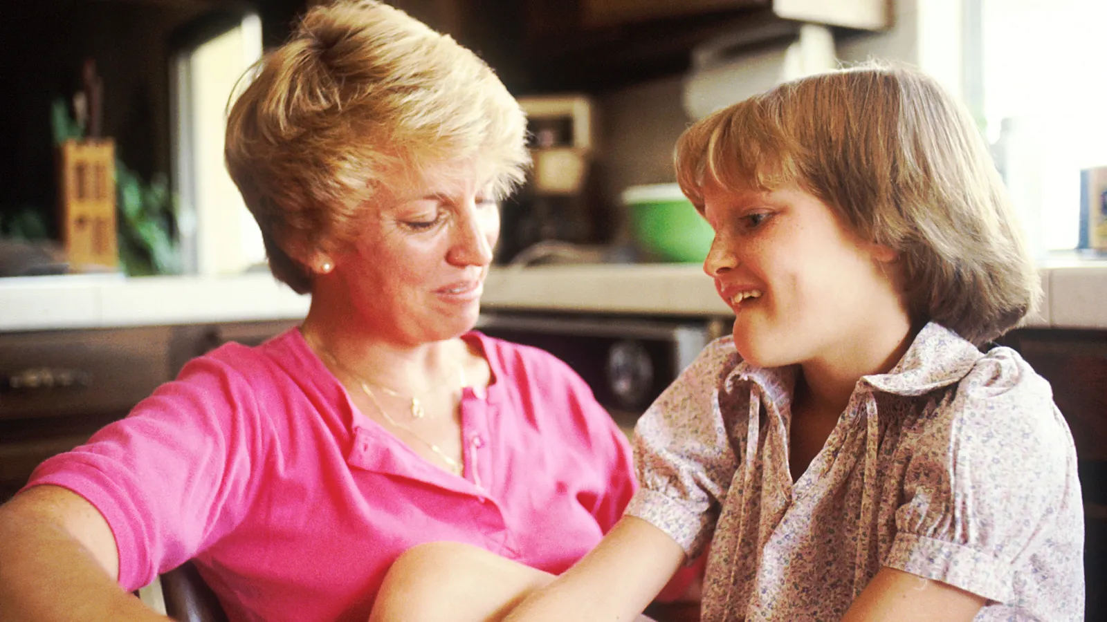Mother and young daughter sitting and talking together in a home kitchen