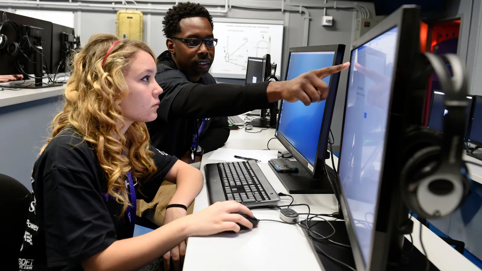 Navy instructor points at a computer screen as a high school student works