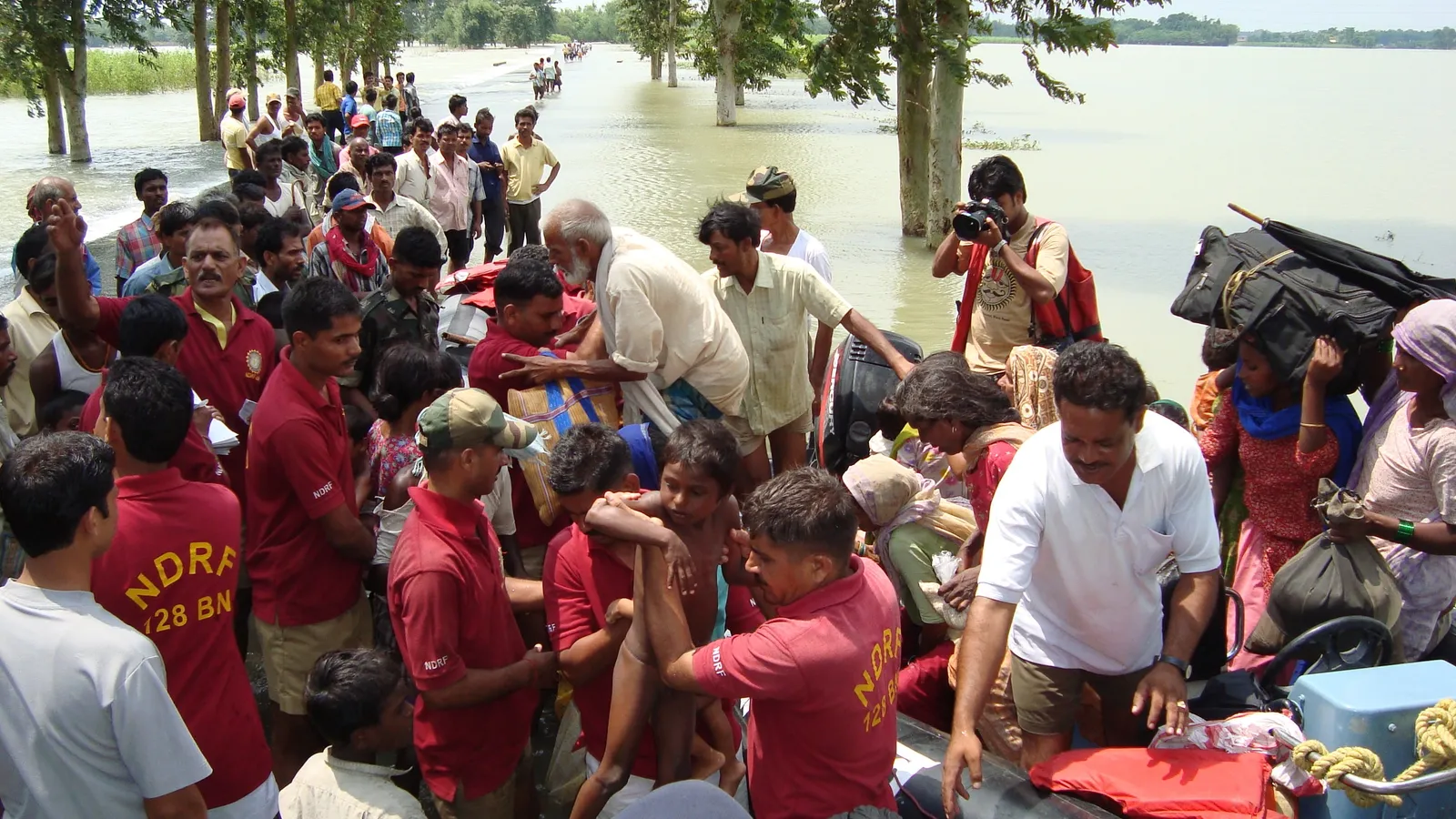 NDRF rescuers in maroon shirts helping flood-hit families off an inflatable boat in India
