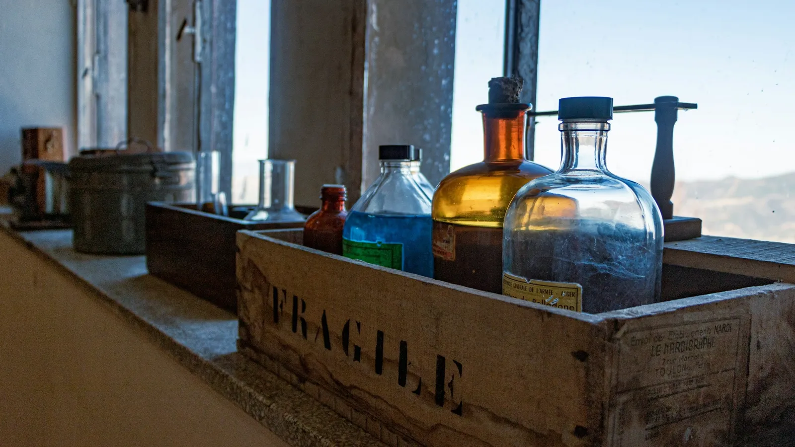 Old glass chemical bottles in a wooden crate by a window