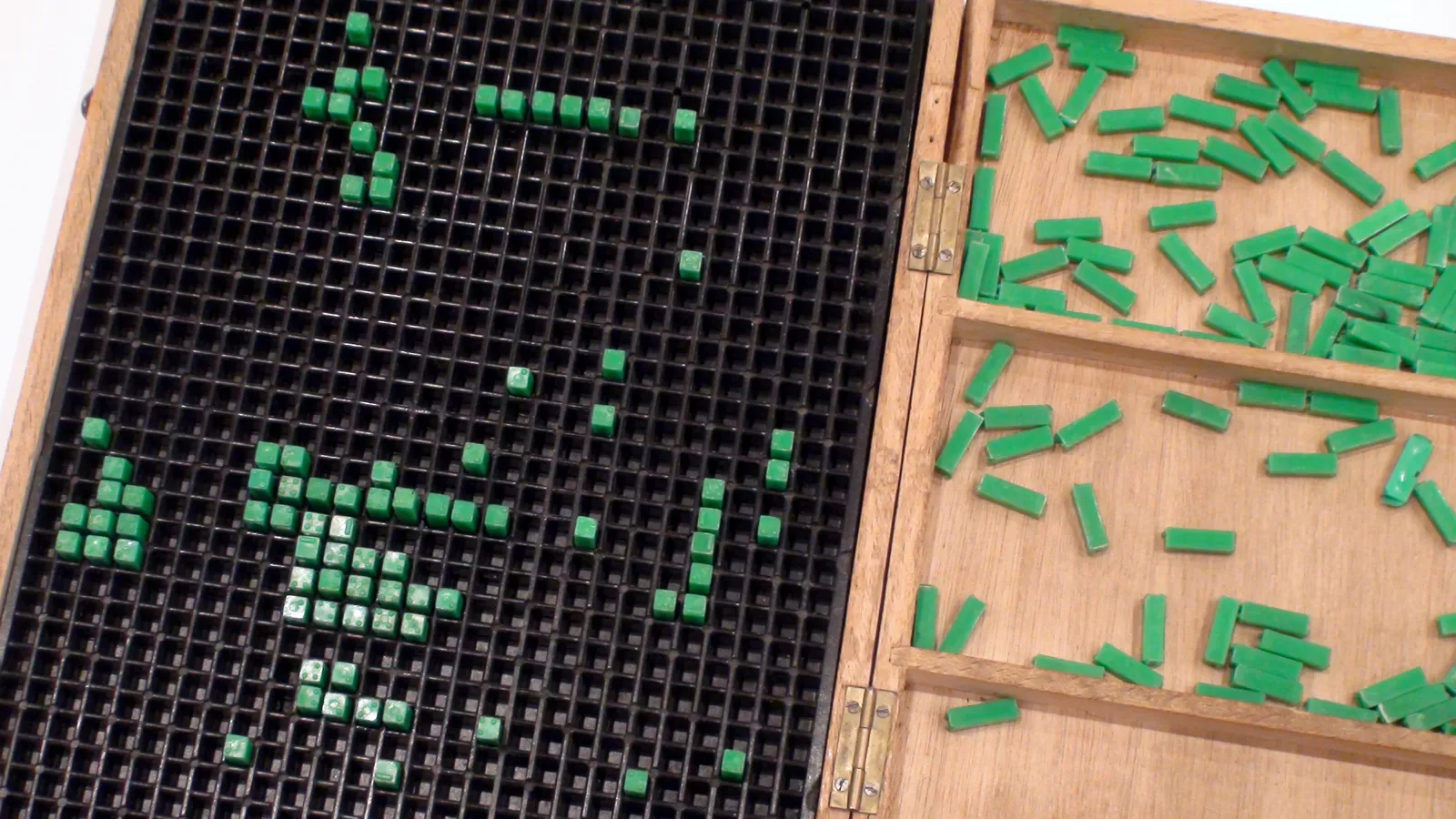 Open wooden box with green braille number pieces set into a black grid for maths