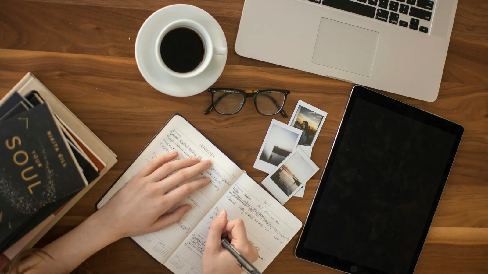 Overhead view of a hand writing in a notebook next to coffee and a laptop