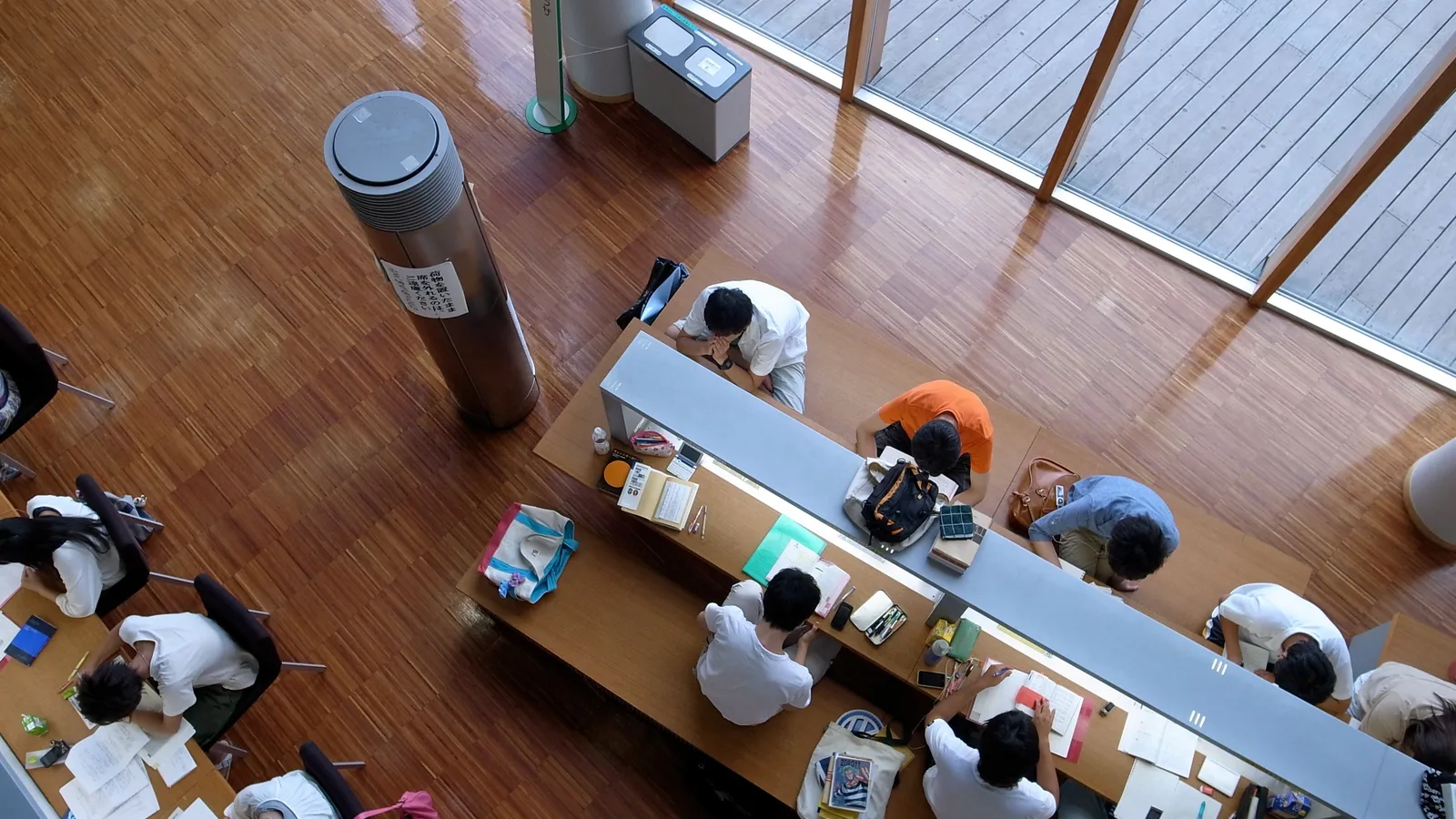 Overhead view of students studying at long library desks with books, notes and phones