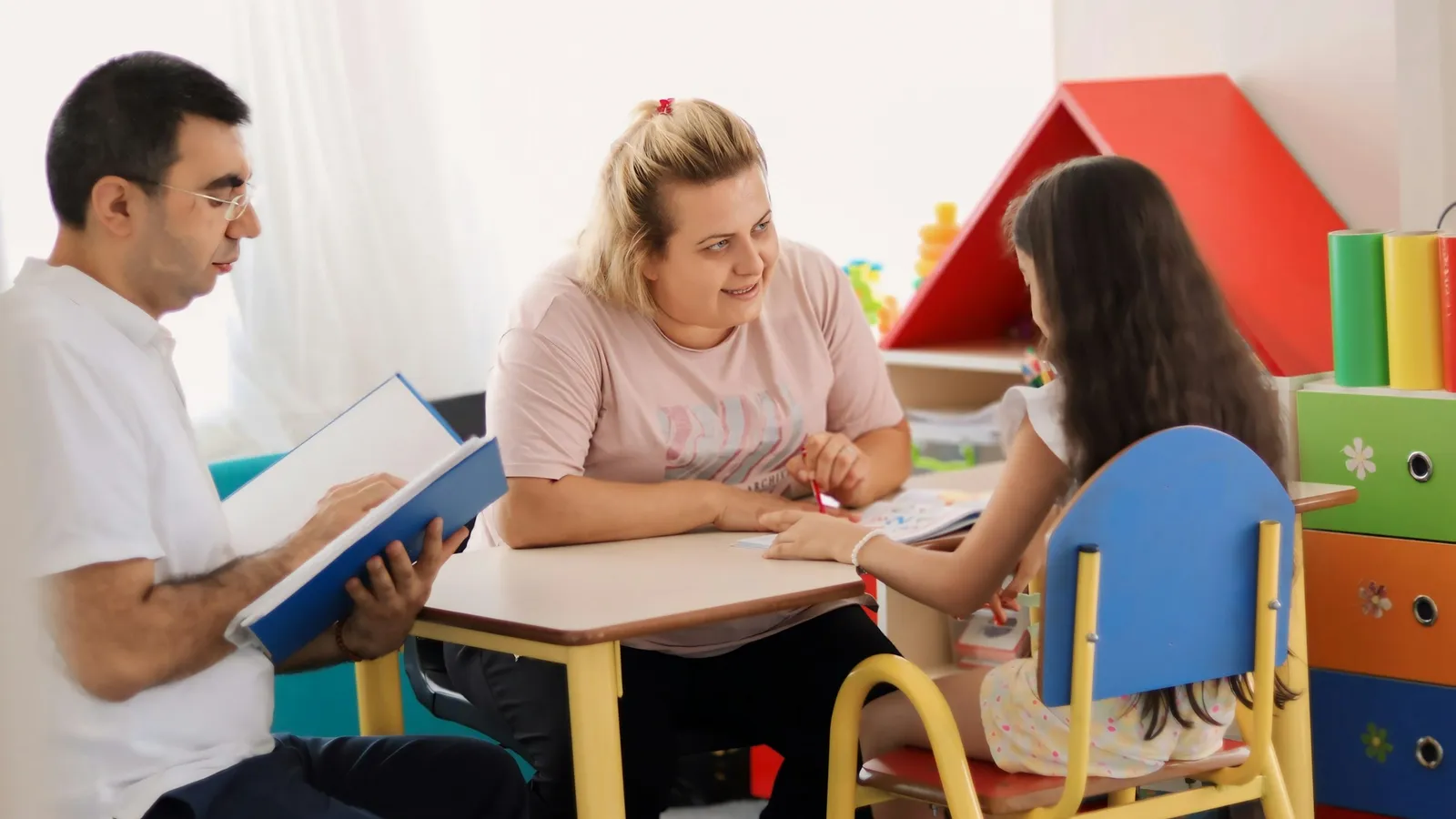 Parents and a teacher talking with a child at a classroom table