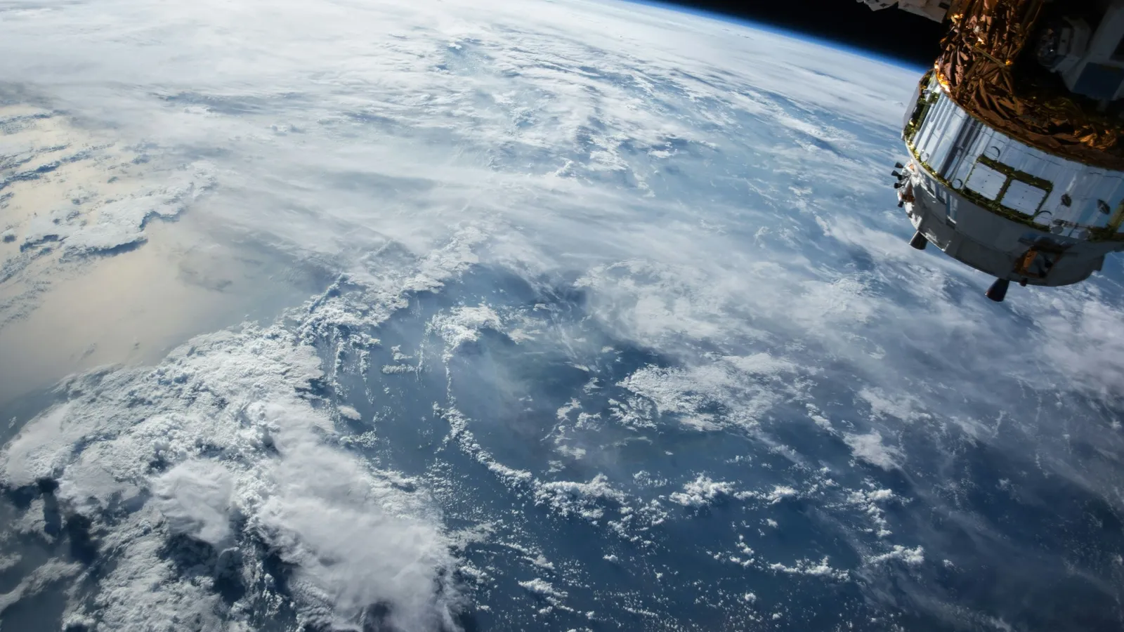 Part of a spacecraft orbiting above Earth, with clouds and ocean below