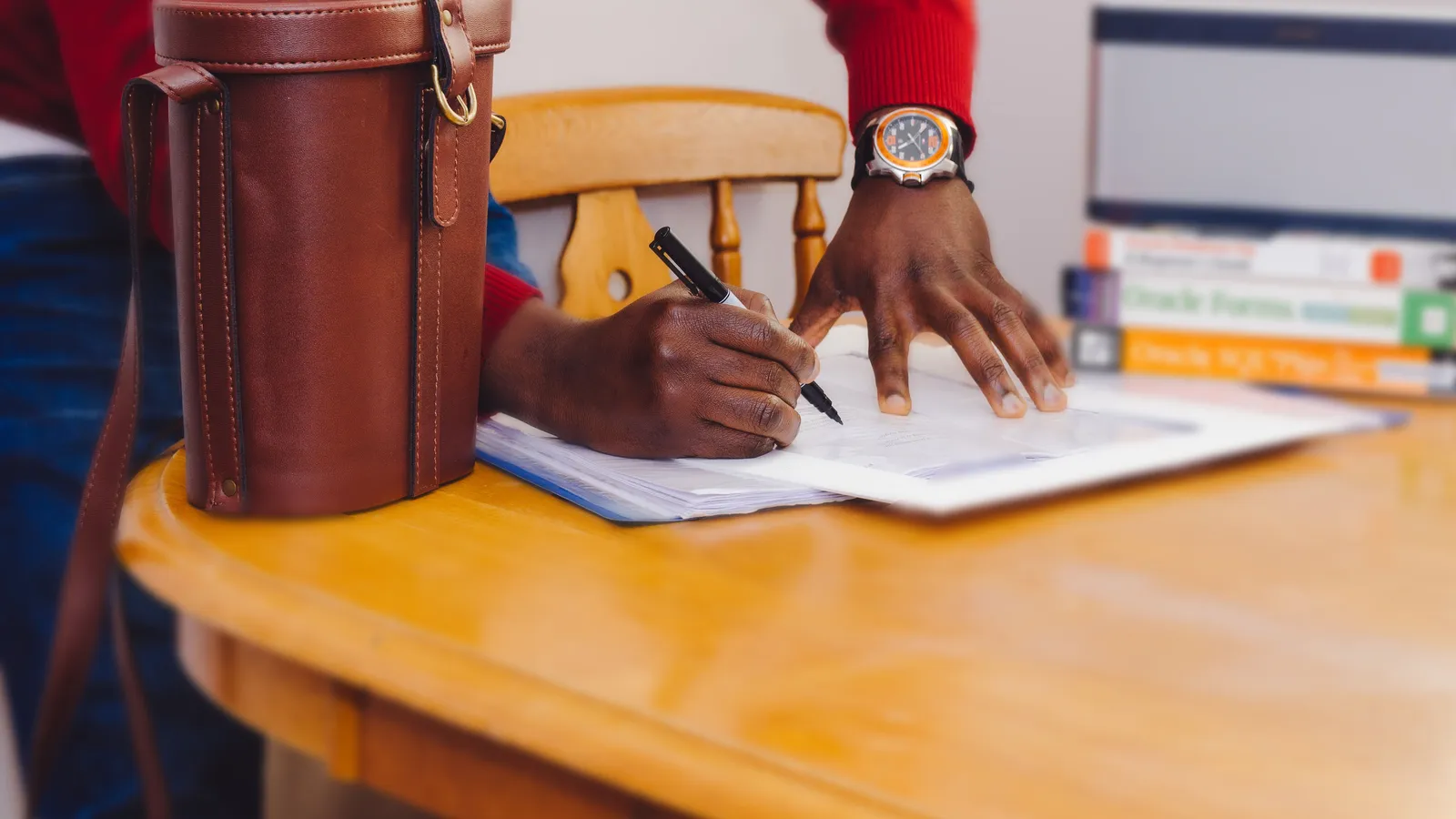 Person in a red sweater writing on printed papers at a wooden table