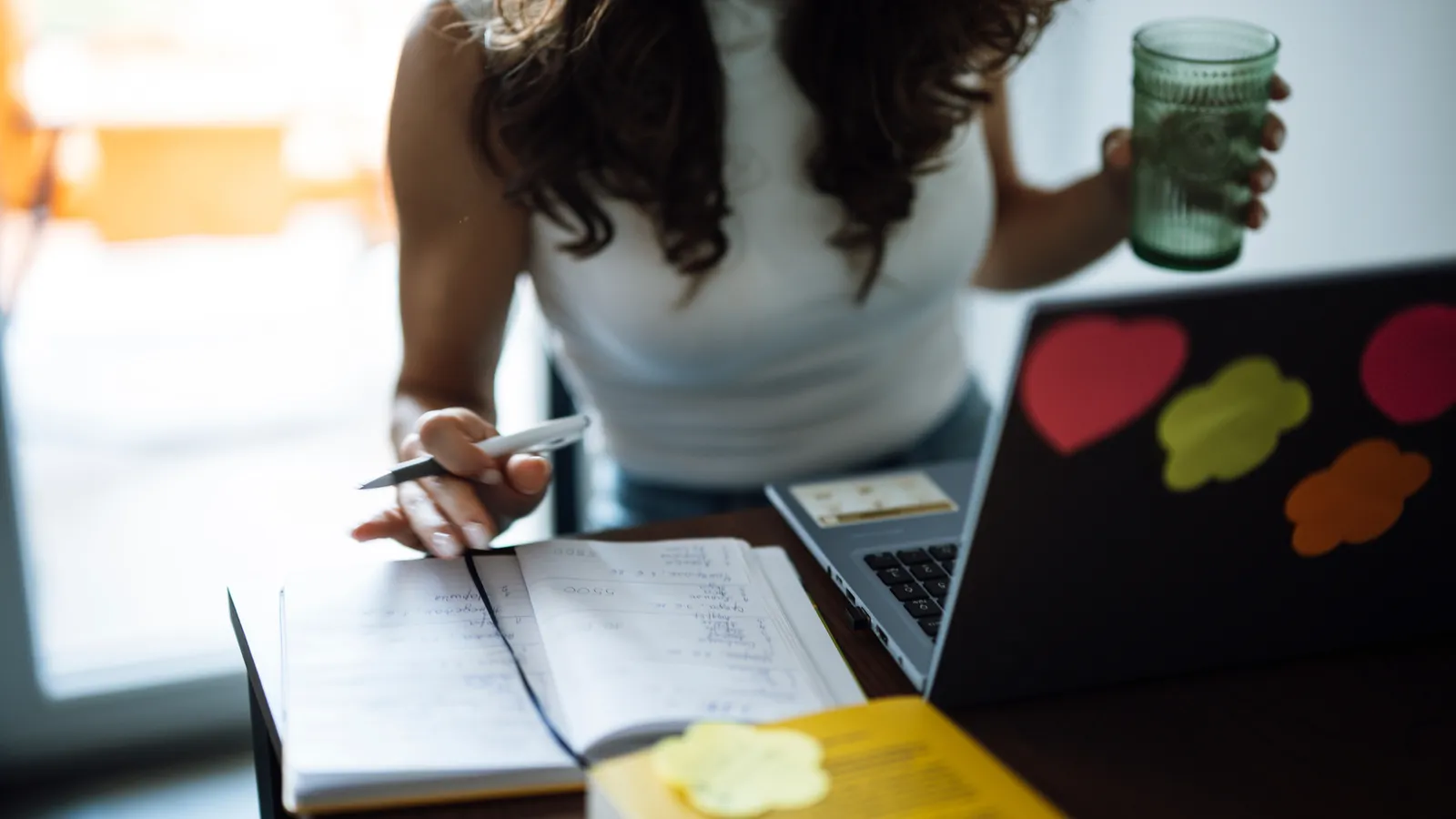 Person writing notes in an open notebook beside a laptop on a desk