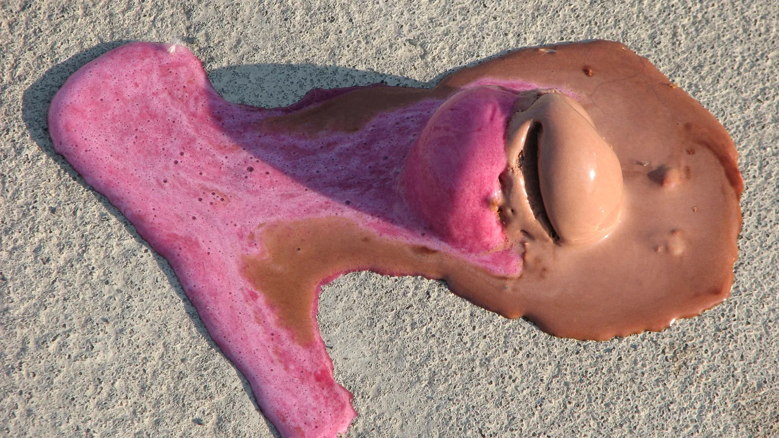 Pink and chocolate ice cream scoops melting into a puddle on concrete
