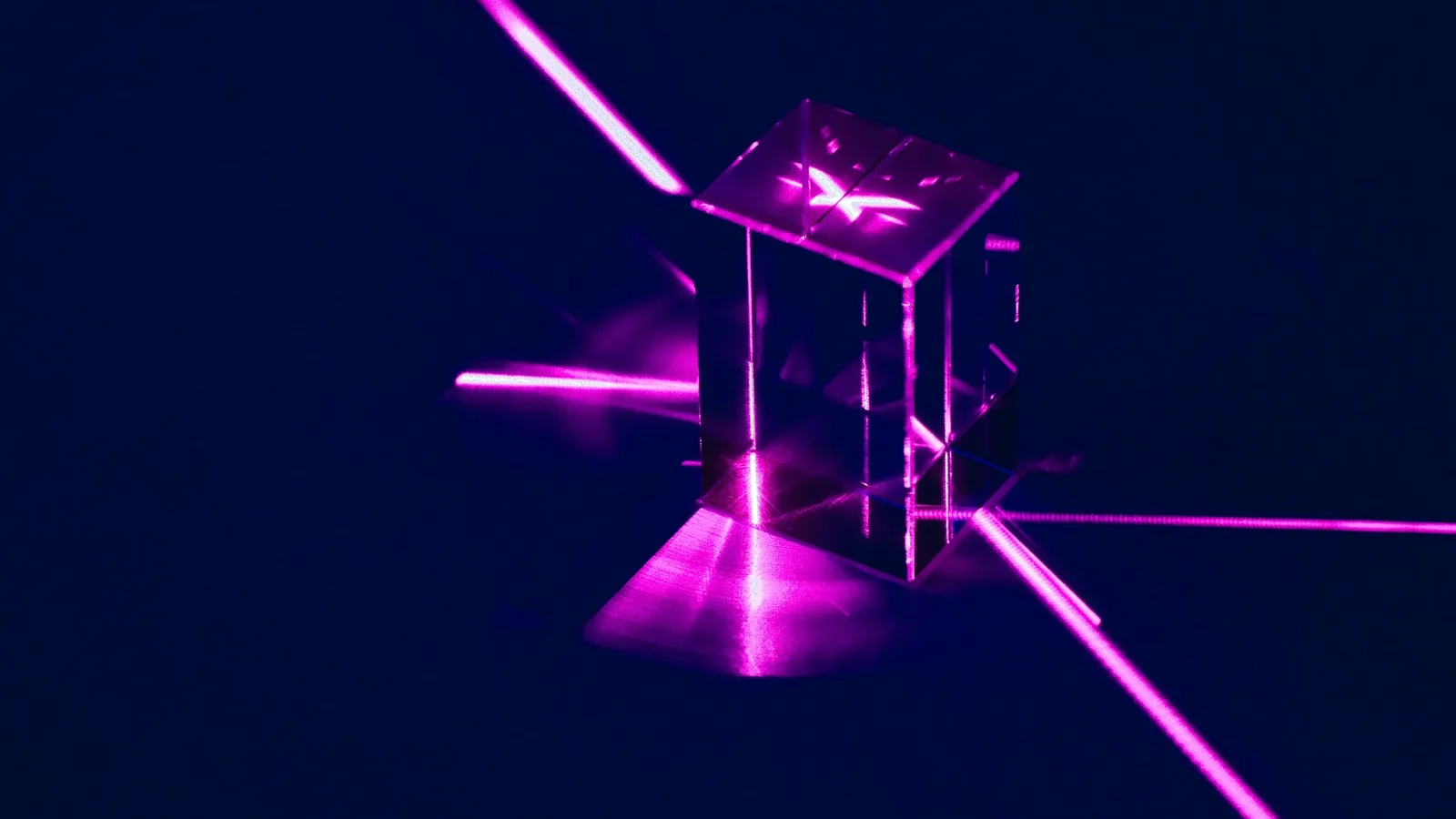 Pink laser beams splitting as they pass through a glass cube