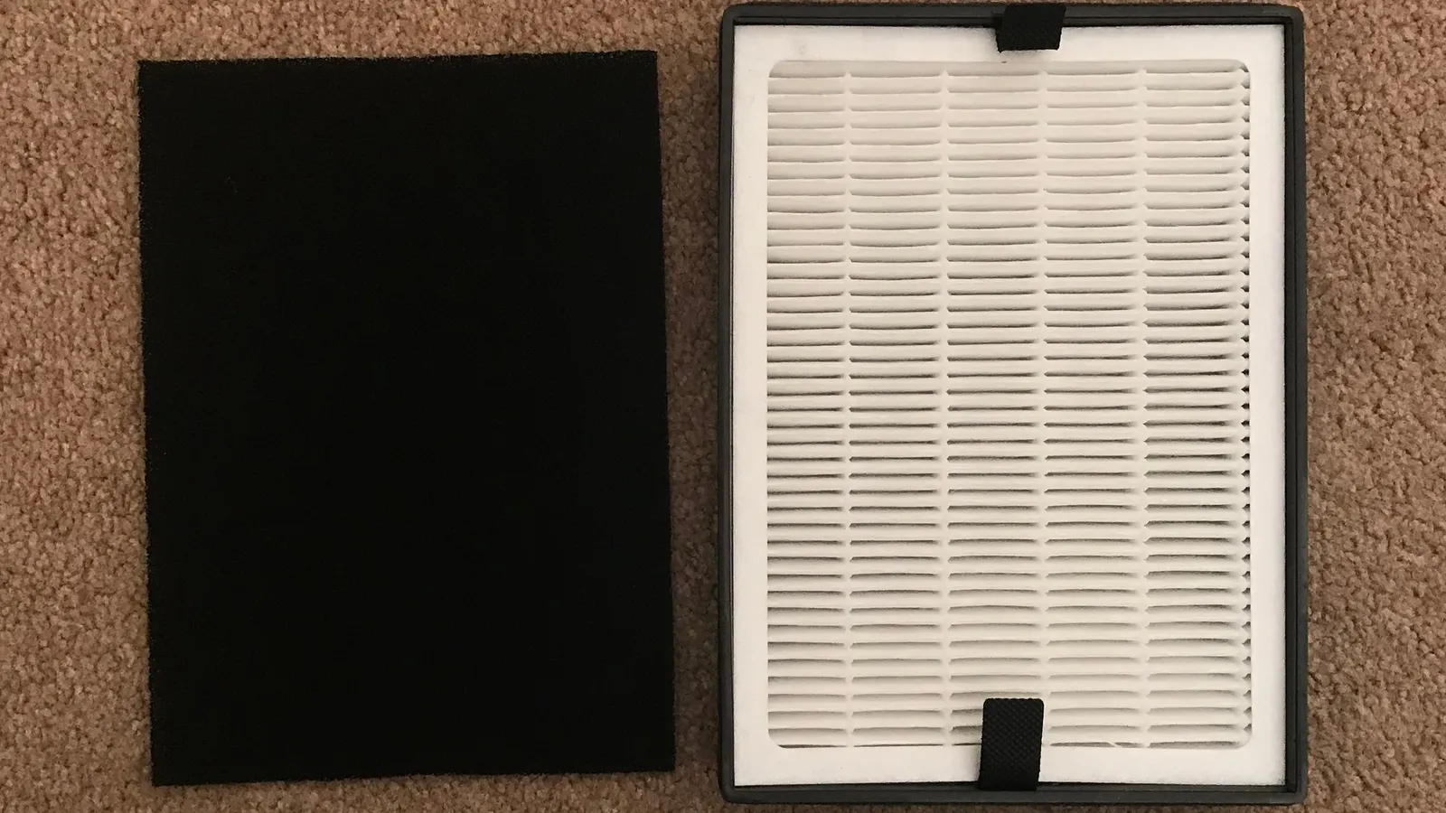 Pleated white HEPA filter beside a black activated carbon sheet on carpet