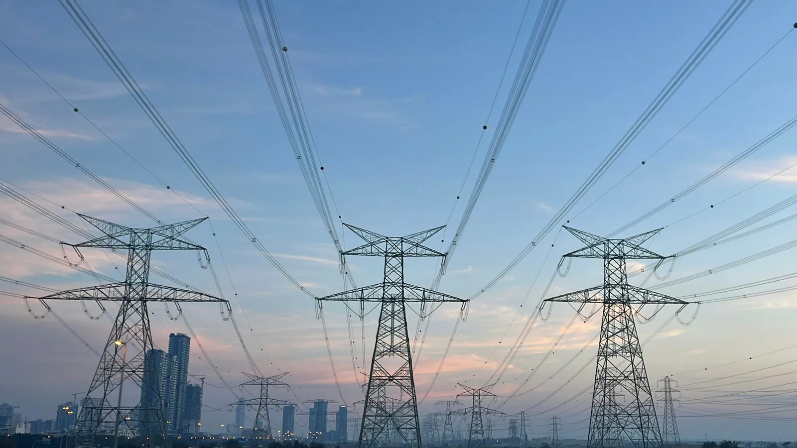 Power lines running between pylons towards a city at dusk