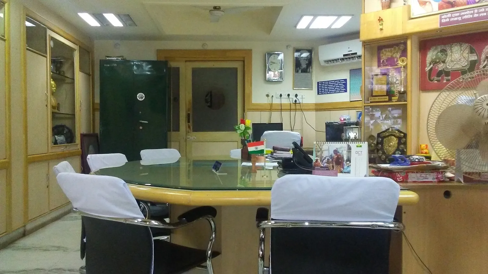 Principal's office in an Indian school with a glass-topped desk, Indian flag, chairs and trophy shelves