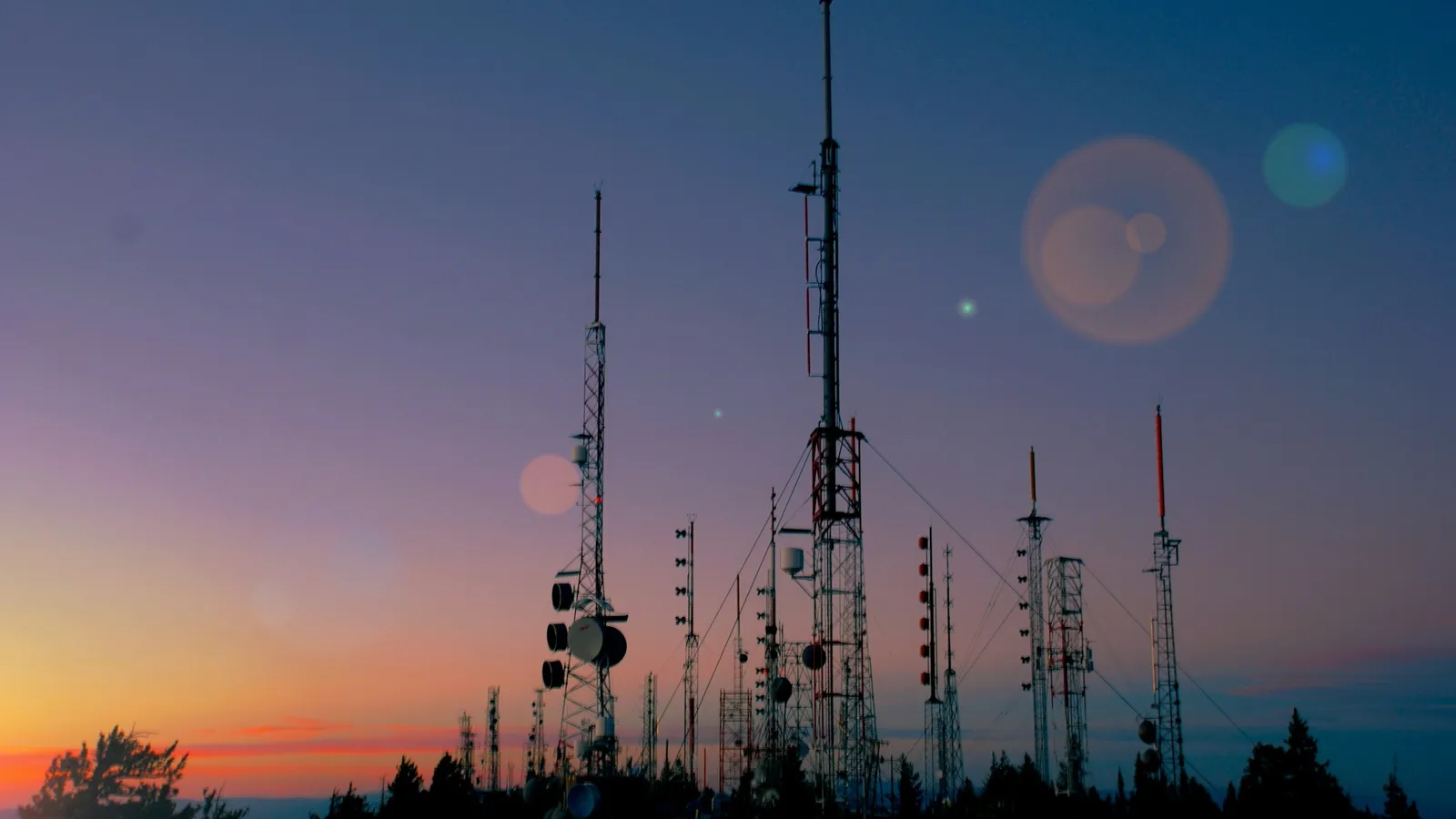 Radio and communication masts silhouetted on a hilltop at dusk