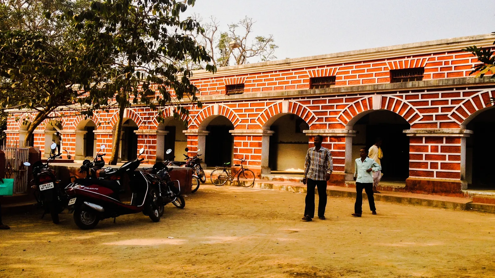 Red-brick arched tehsil office in Khordha, Odisha, with parked scooters and visitors