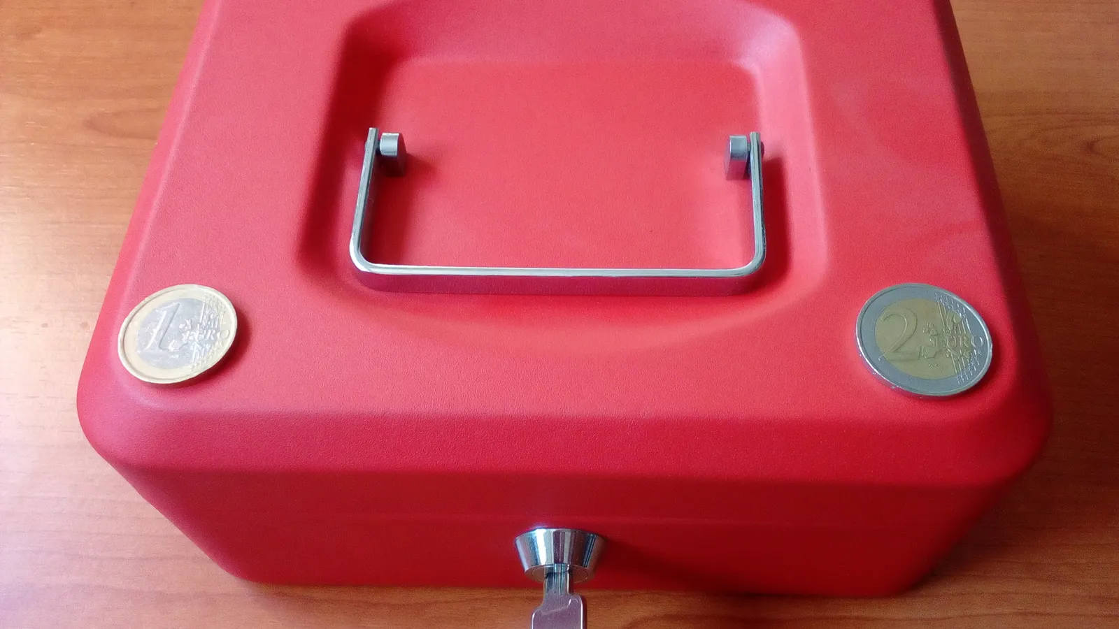 Red cash box with a key in its lock and two coins on top